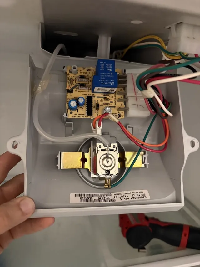 Hand holding an opened refrigerator control housing with a circuit board and a thermostat inside