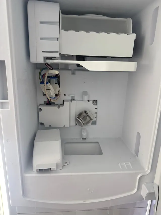 Ice maker compartment inside a refrigerator door, opened to show the ice maker, its wiring and housing