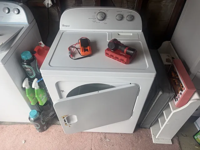 White Whirlpool dryer in a garage with its door open, a multimeter and a cordless drill resting on top